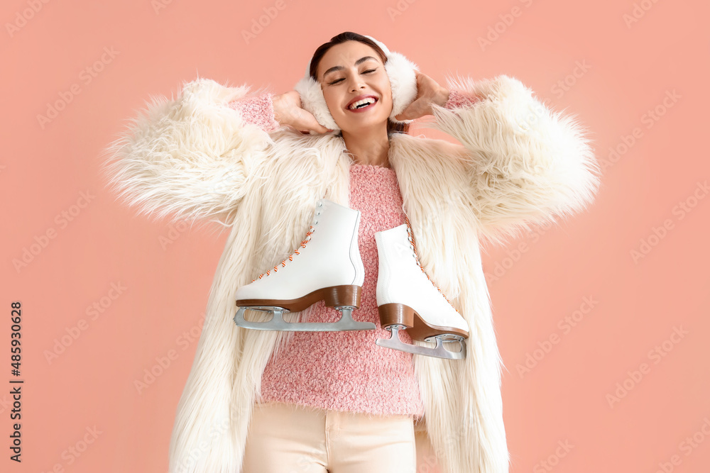 Happy young woman in warm clothes with ice skates on pink background