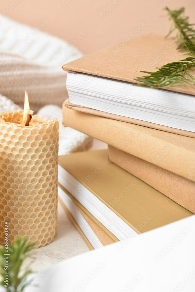 Stack of books and burning candle on table, closeup