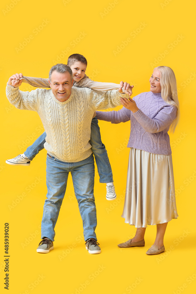 Little boy with his grandparents in warm sweaters having fun on yellow background