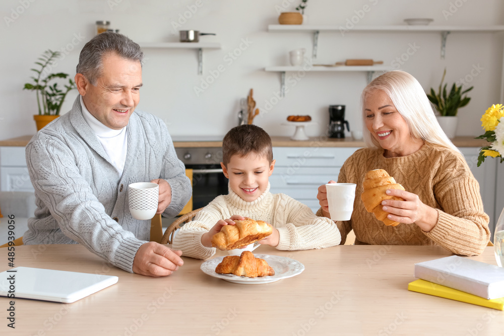 Little boy and his grandparents with cups of cocoa eating croissants at home