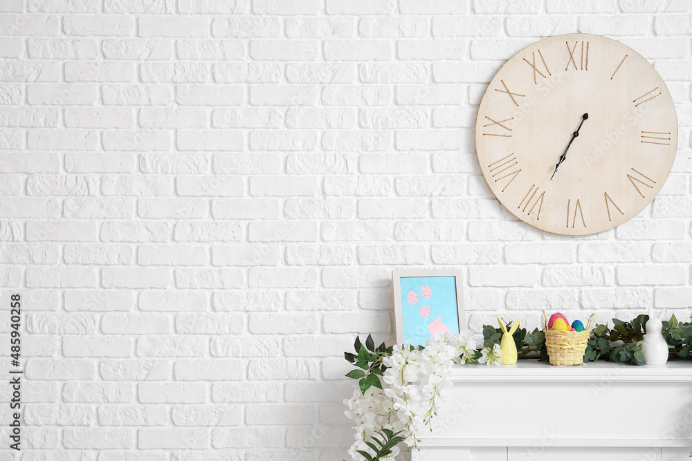 Painting with flowers, eucalyptus and Easter eggs in basket on mantelpiece near white brick wall