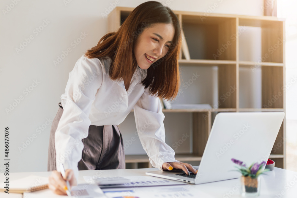 Happy smiling Asian woman in office working with laptop on office desk.