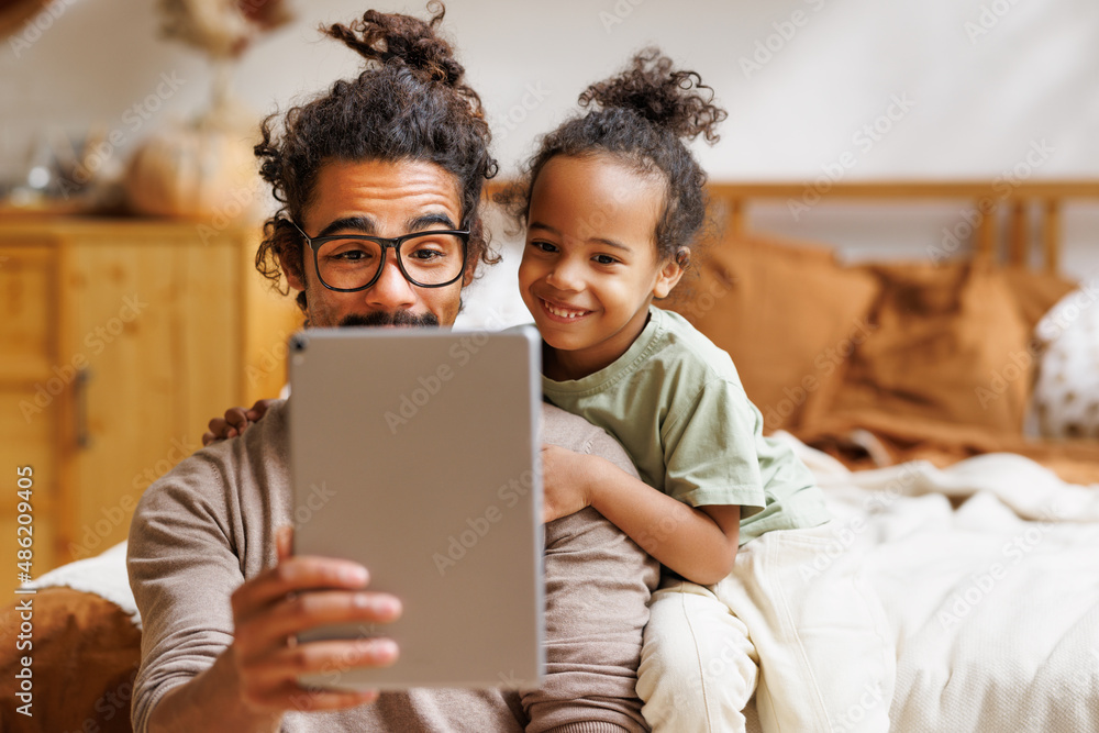 Happy african american family little son with dad watching funny videos on tablet together at home