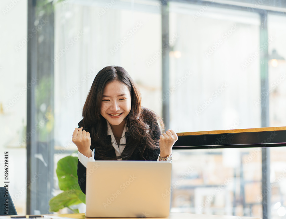 兴奋的亚洲女人坐在办公桌前，兴高采烈地中了网上彩票，快乐的黑人女人喜出望外地得到了妈妈