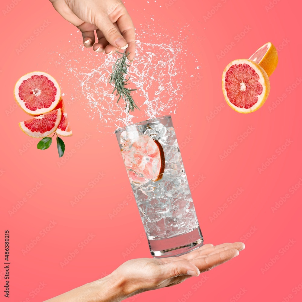 Woman hand support glass of grapefruit drink with splash, juice grapefruit slices falling in glass.