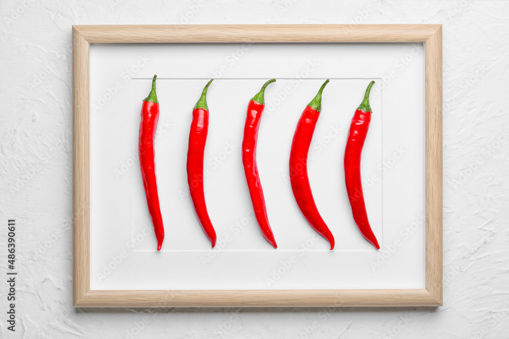 Composition with hot chili peppers and blank frame on light background