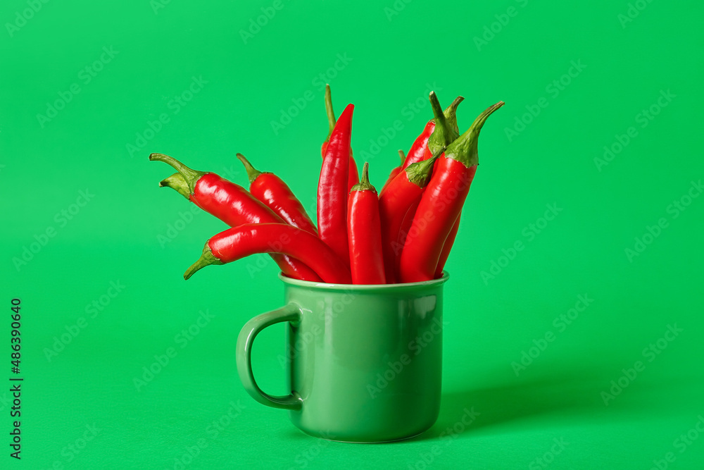 Mug with hot chili peppers on green background