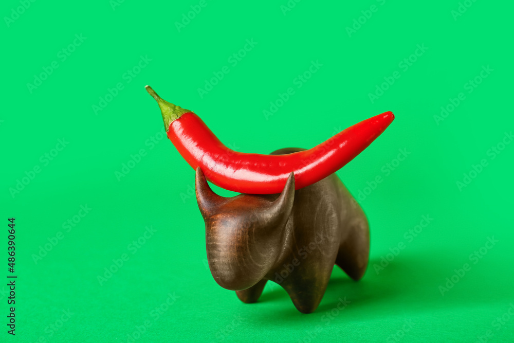 Wooden bull with hot chili pepper on green background