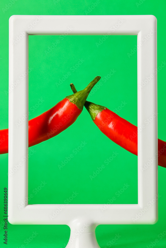 Frame and hot chili peppers on green background