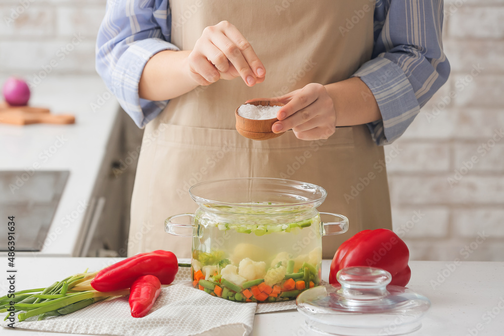 Woman adding salt in tasty dietary soup on table in kitchen