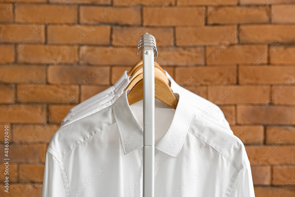 Rack with clean shirts near brick wall