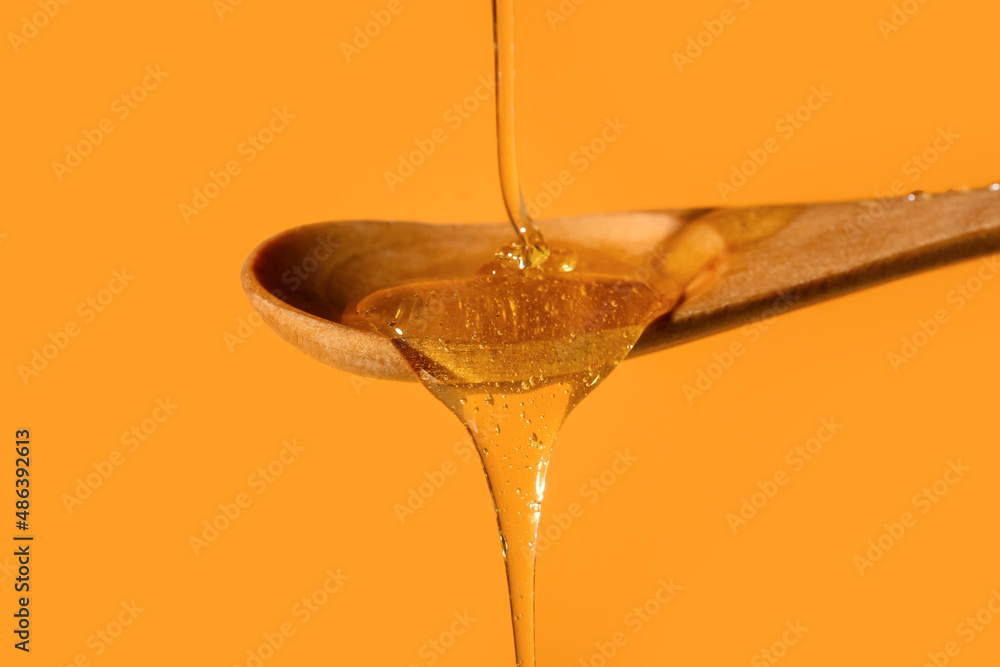 Honey dripping into wooden spoon on color background, closeup