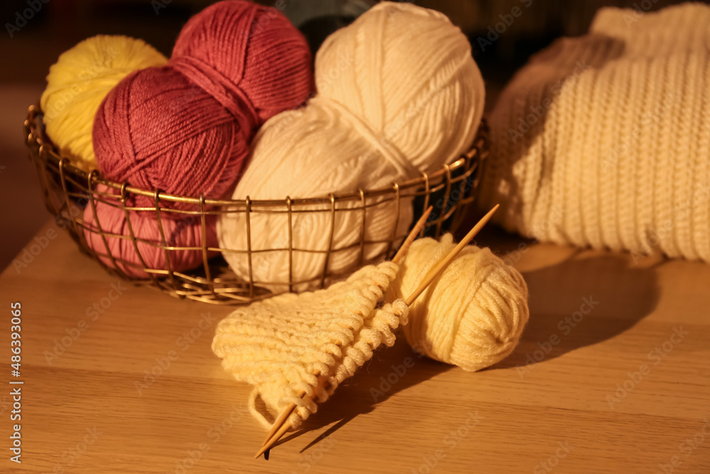 Basket with knitting yarn and needles on wooden table in room