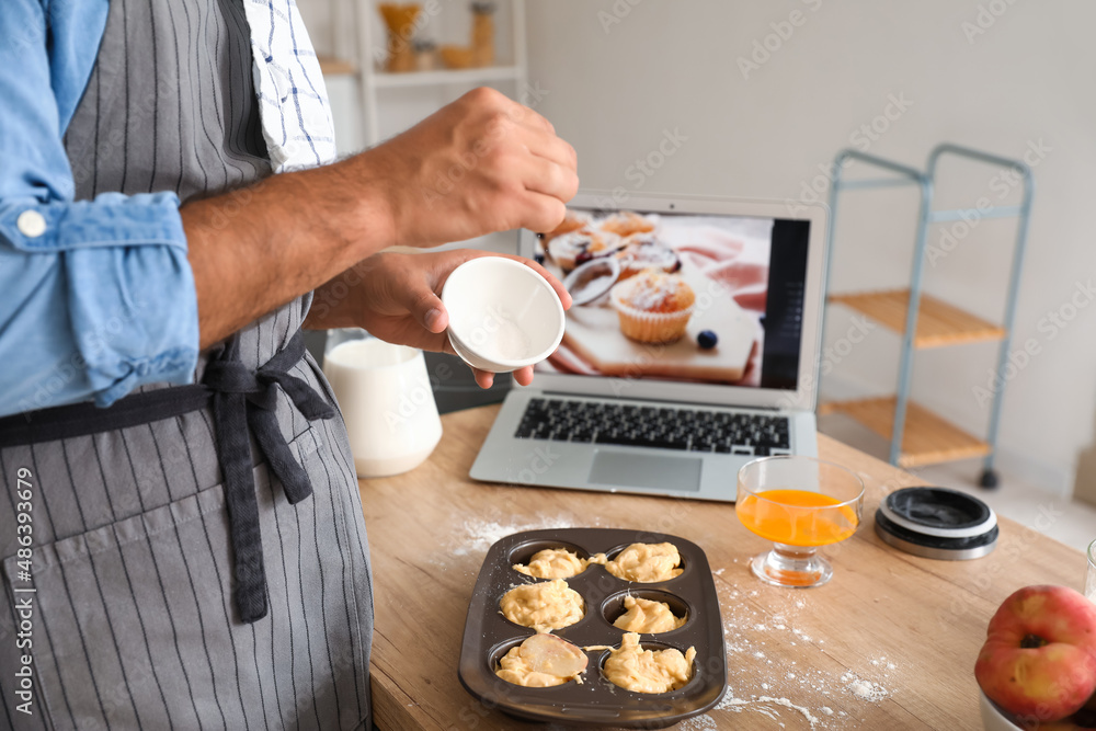 Young man preparing peach muffins while following video tutorial in kitchen