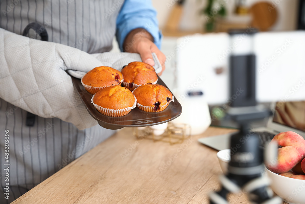 Handsome man with tasty peach muffins recording video in kitchen