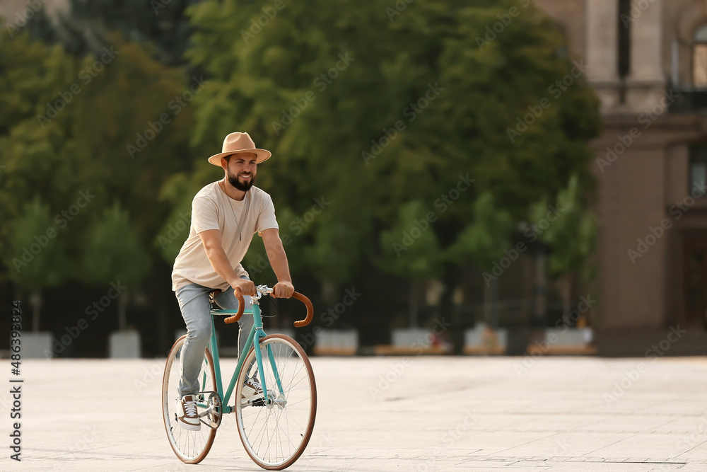 Handsome bearded man riding bicycle on city square