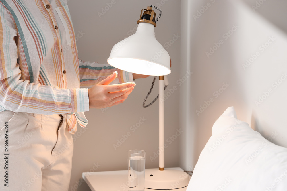 Woman changing light bulb in lamp near bed at home