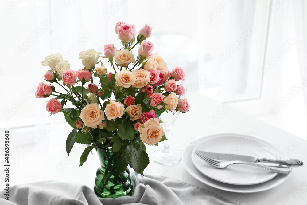 Vase with beautiful roses on served table in light room