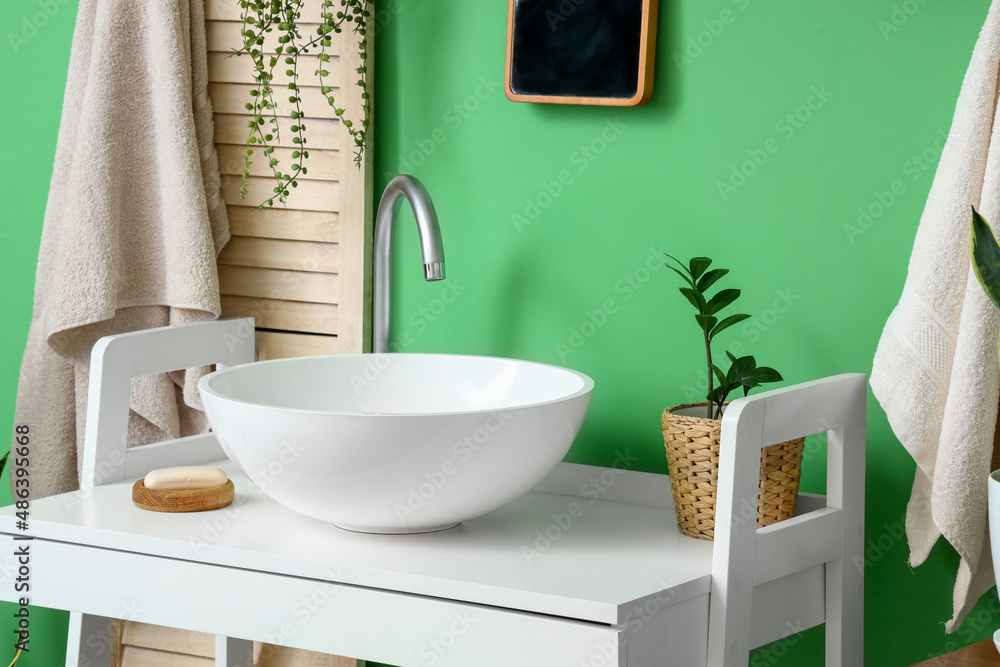 Table with white sink, houseplant and soap near green wall