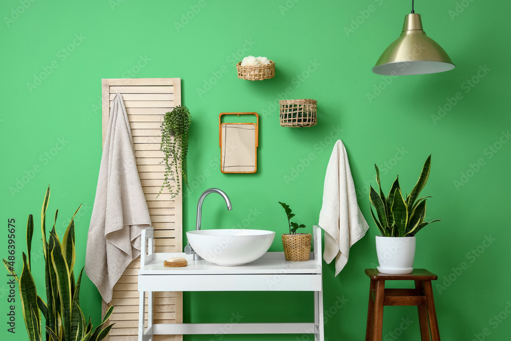 Interior of stylish bathroom with white table, sink and houseplants