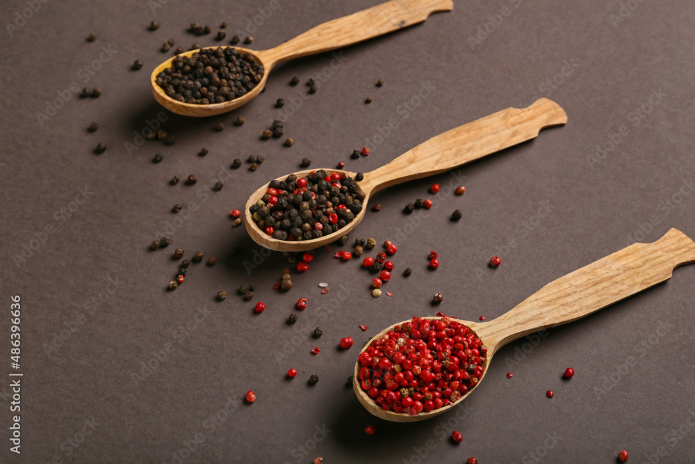 Wooden spoons with different peppercorns on dark background