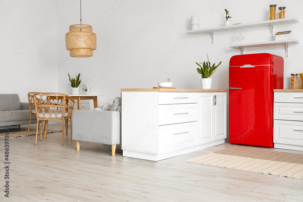 Interior of light kitchen with white counters, red fridge and dining table