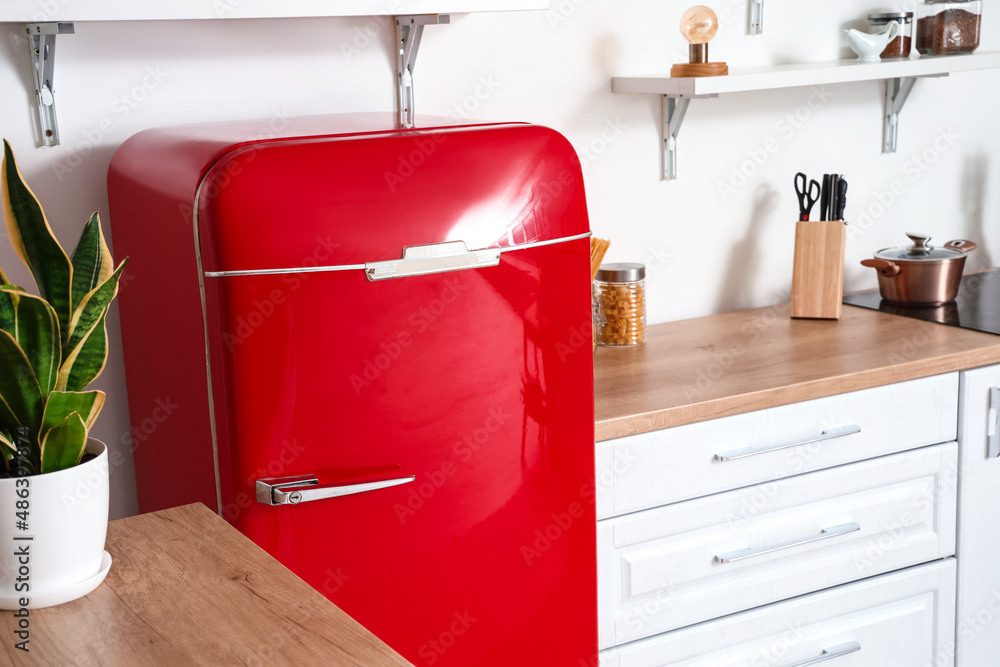 Stylish red fridge near light wall in kitchen