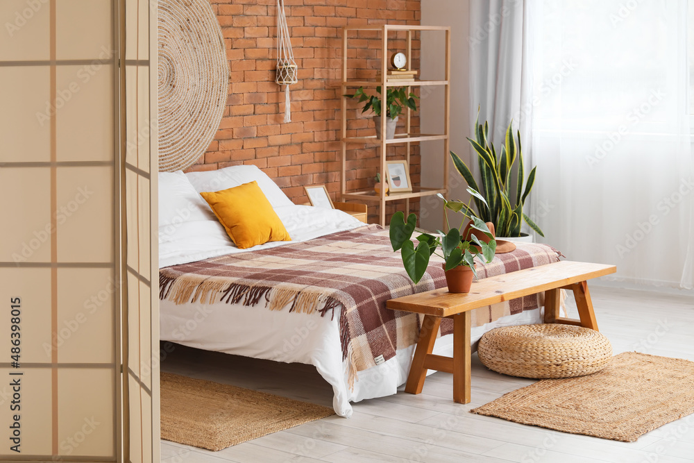 Interior of stylish bedroom with folding screen and wooden bench