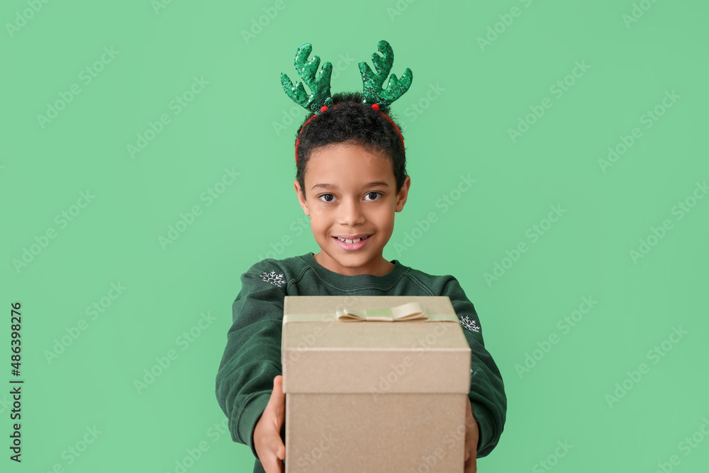 Cute little African-American boy with Christmas box on color background