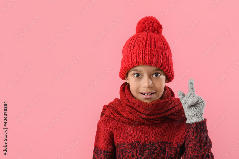 Cute little African-American boy in winter clothes and with raised index finger on color background