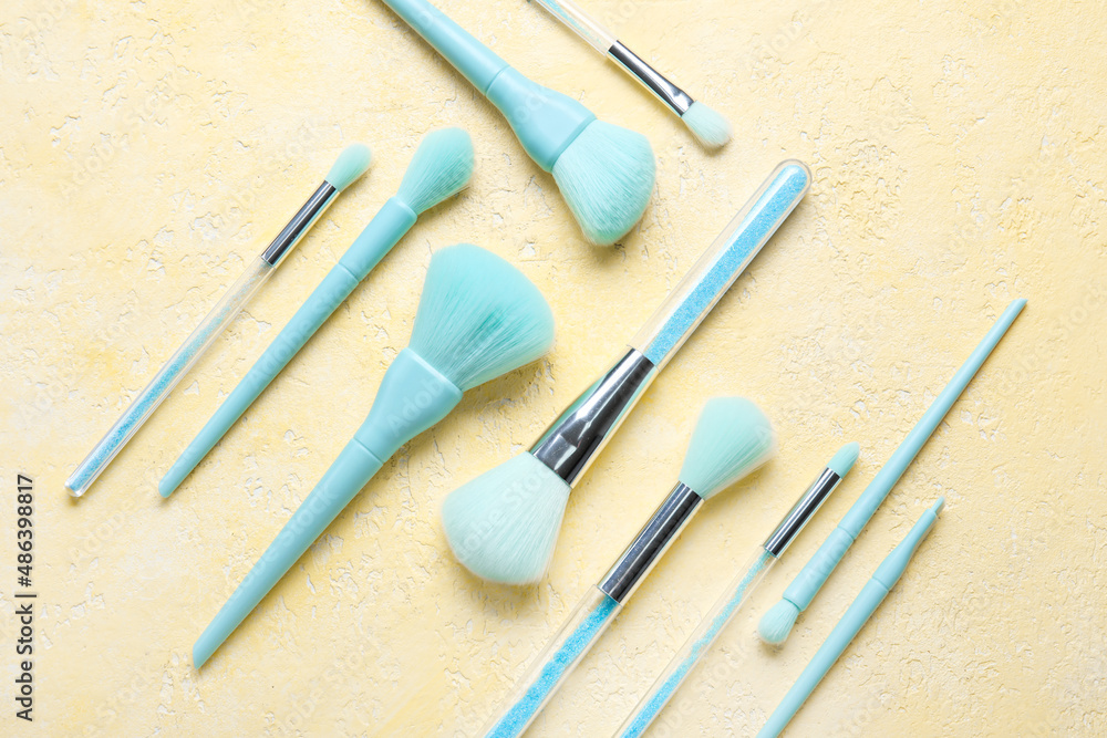 Set of blue makeup brushes on yellow background