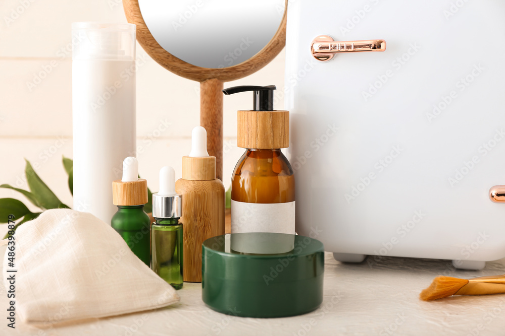 Small refrigerator with cosmetic products on light table, closeup