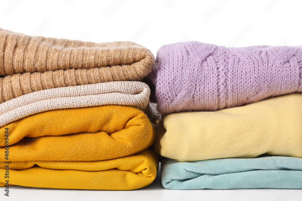 Stacks of stylish female sweaters on white background, closeup