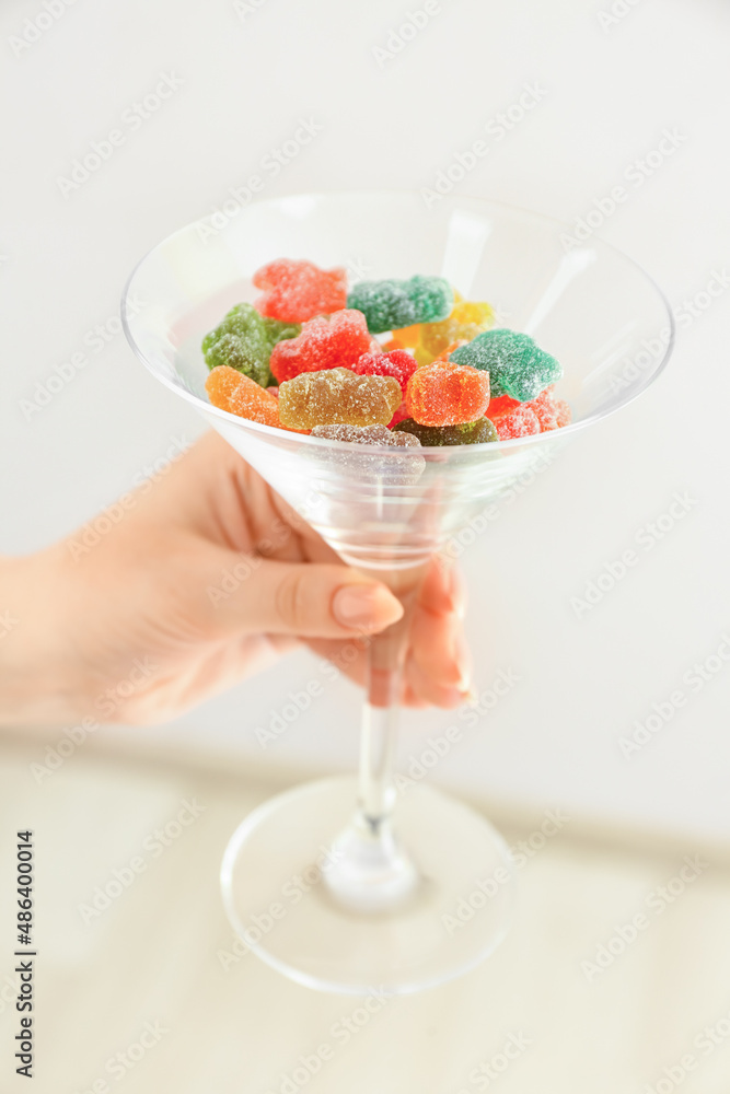 Woman holding glass with jelly bears on light background