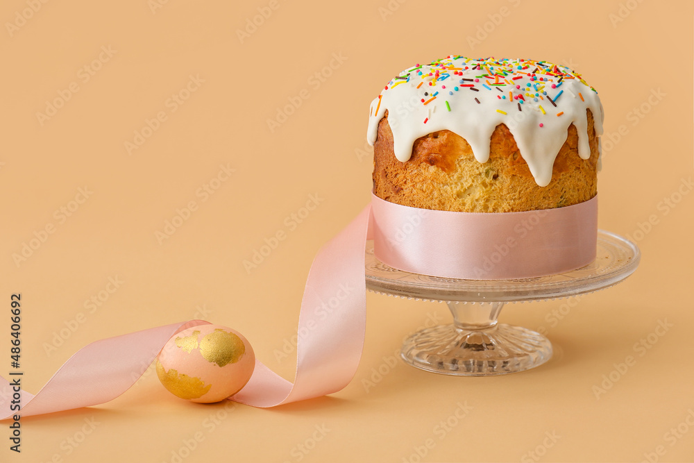 Dessert stand with delicious Easter cake and egg on beige background