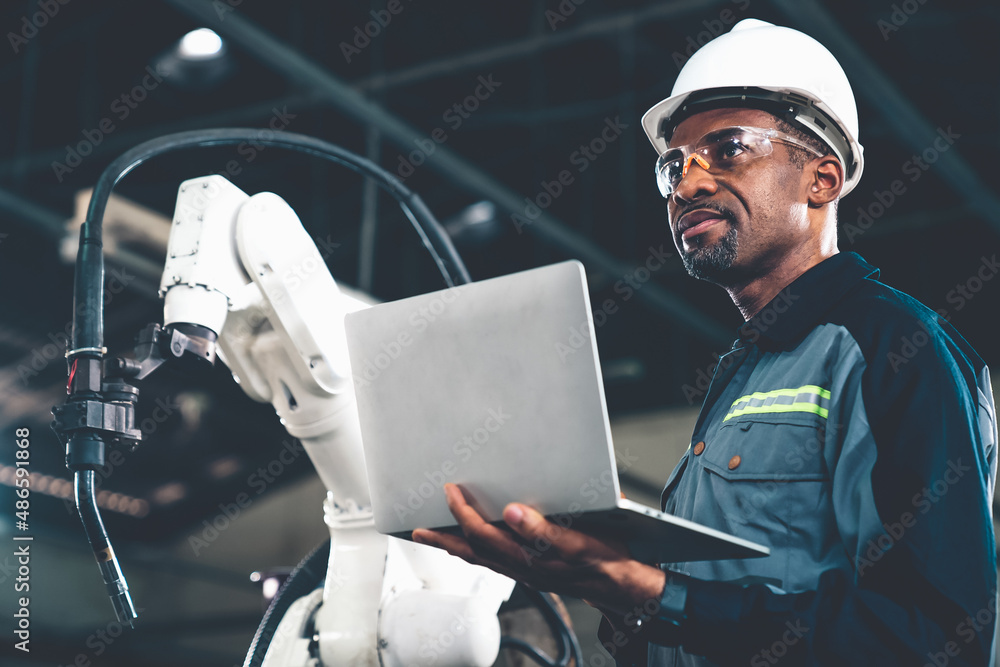 African American factory worker working with adept robotic arm in a workshop . Industry robot progra