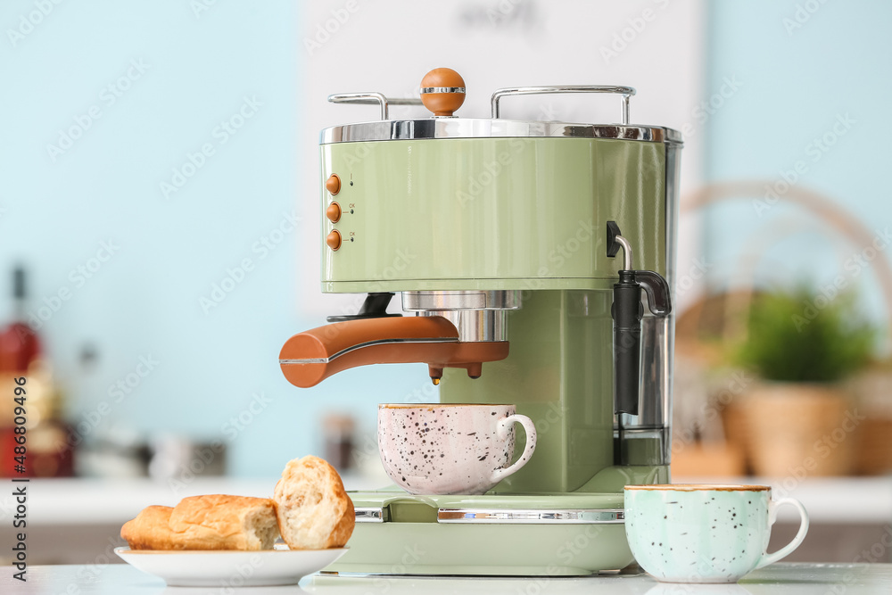 Modern machine with cup of fresh coffee on table in kitchen