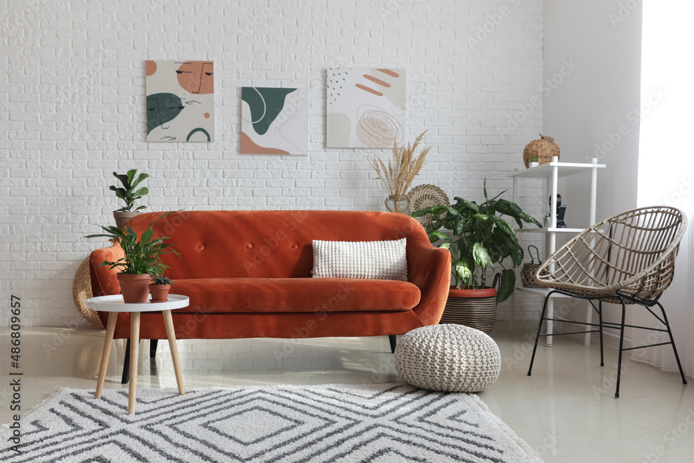 Stylish orange sofa with houseplants in modern interior of living room