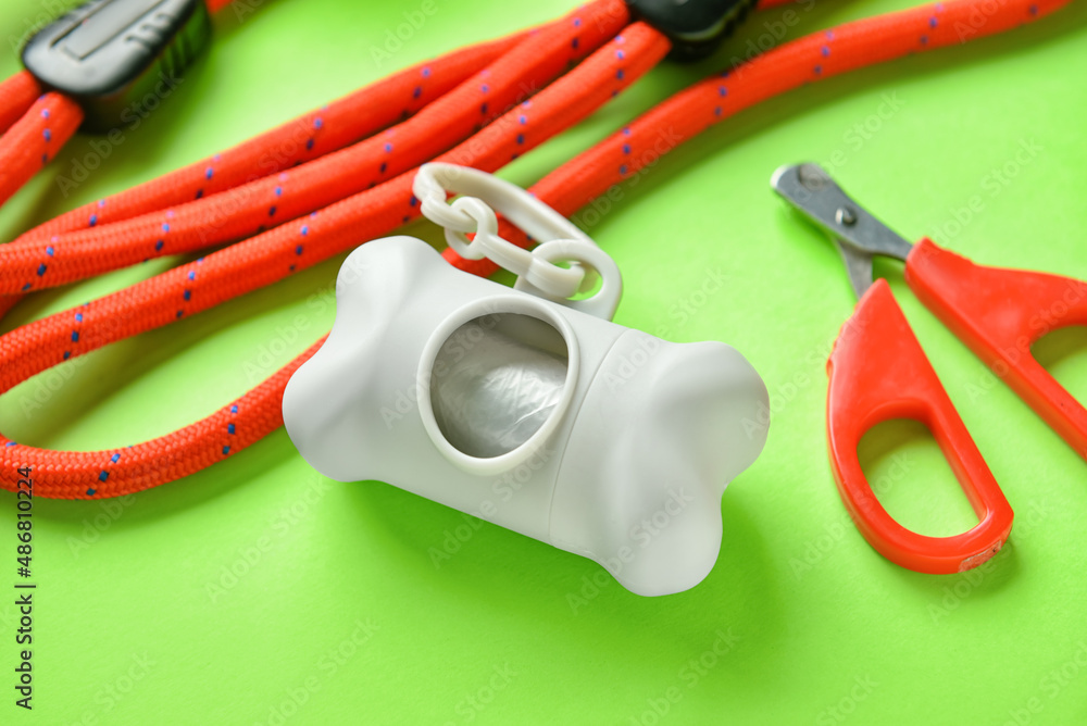 Dispenser with pet waste bags, nail clipper and leash on green background, closeup