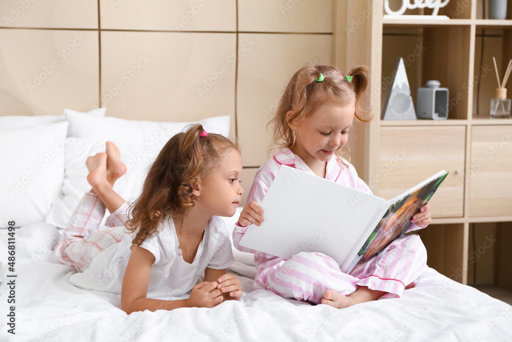 Adorable little sisters with book in bedroom