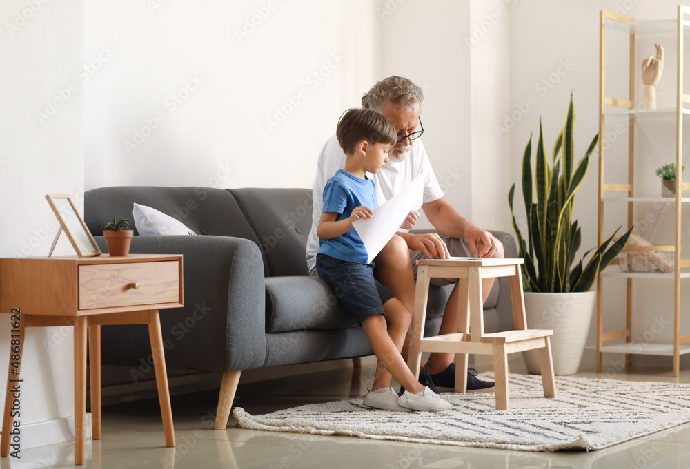 Senior man showing his little grandson how to make paper boat at home