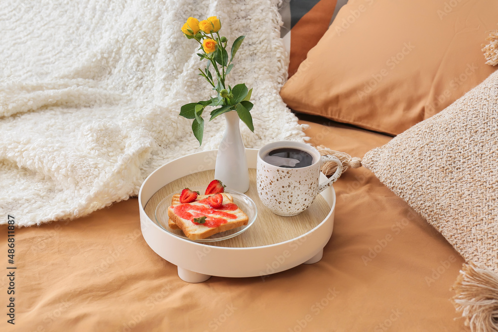 Tray with tasty breakfast and vase with flowers on comfortable bed