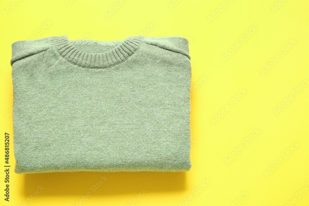 Stylish folded sweater on yellow background