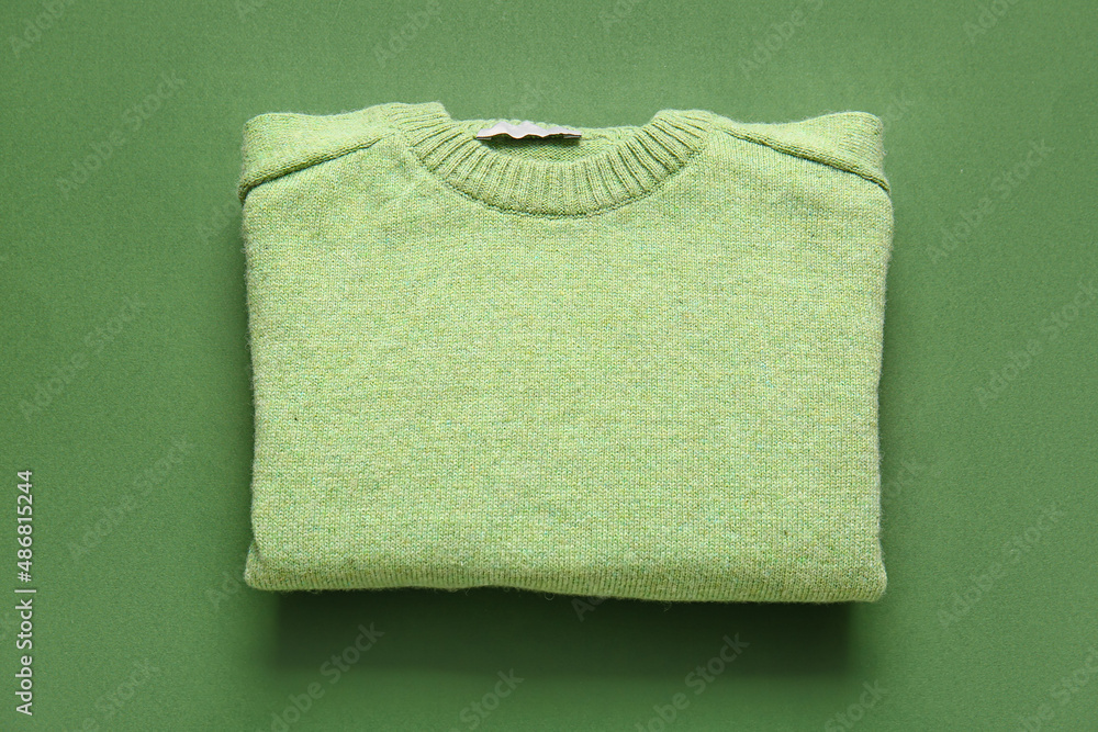 Stylish folded sweater on green background