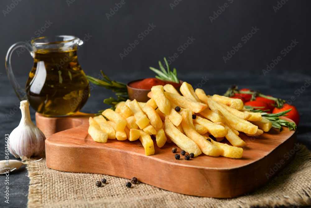 Wooden board with tasty french fries on black background