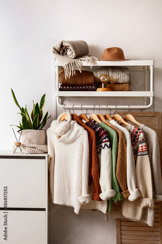 Rack with different stylish knitted sweaters near light wall