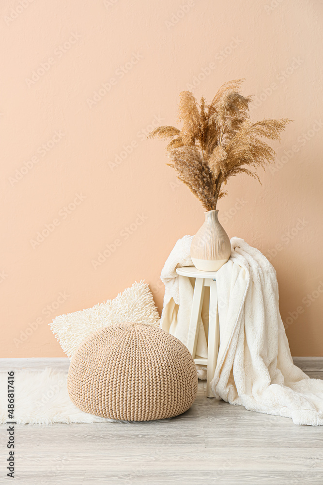 Table with vase, blanket and pouf near beige wall