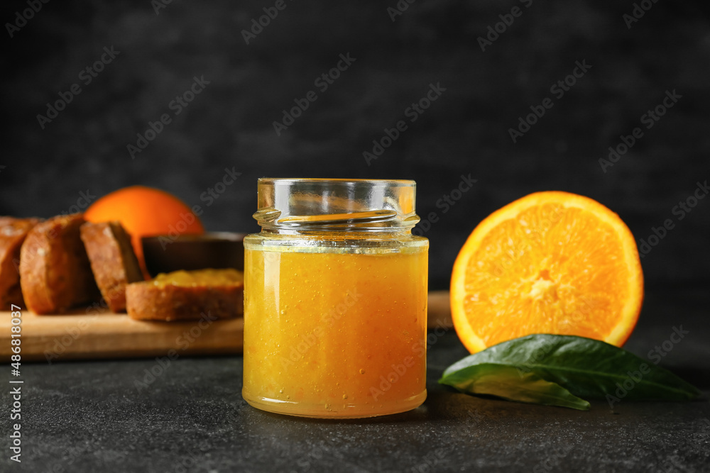 Glass jar of tasty orange jam on dark background