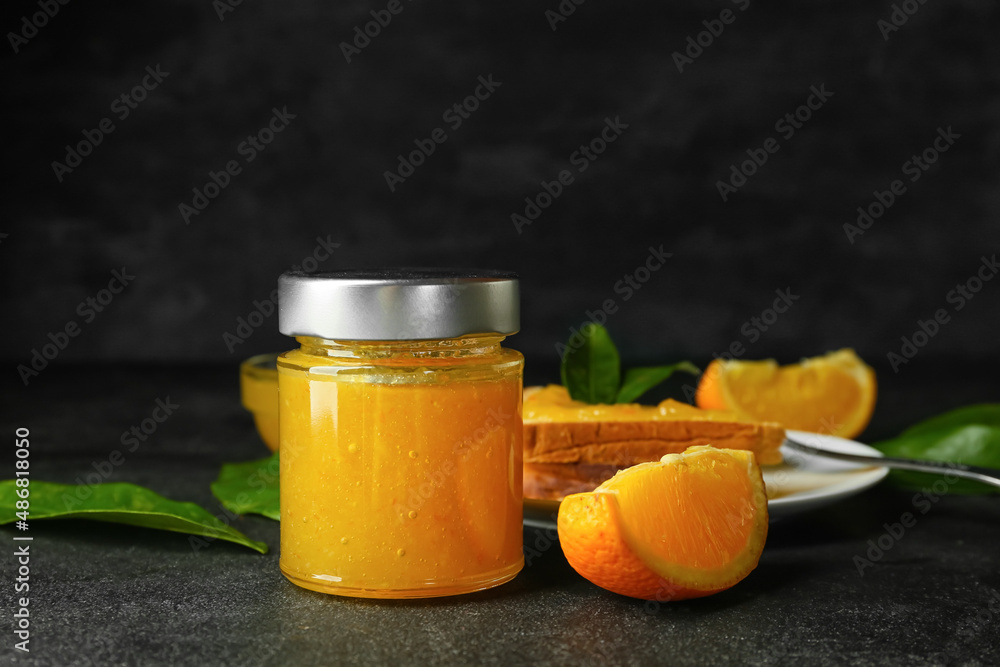 Glass jar of tasty orange jam on dark background