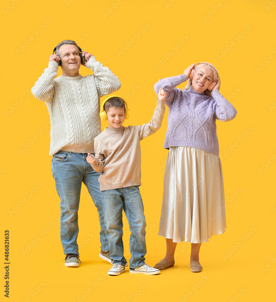 Little boy with his grandparents in warm sweaters and headphones on yellow background